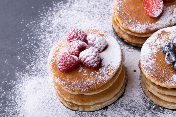High angle close-up of powdered sugar over stacked pancakes with various berry fruits on food slate