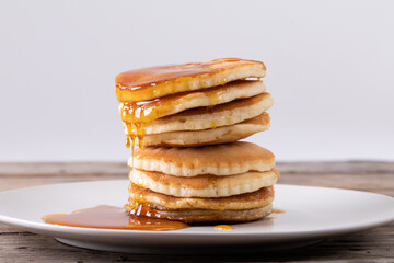 Stack of eight pancakes with syrup served in plate on table against gray background
