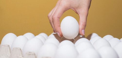 hand takes a white egg from the tray. Background for text Holiday Easter