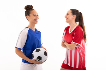 Smiling caucasian and biracial young female soccer players talking standing against white background © wavebreak3