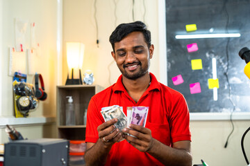 Happy mobile technician counting money at repair shop - concept of business profit, earnings and...
