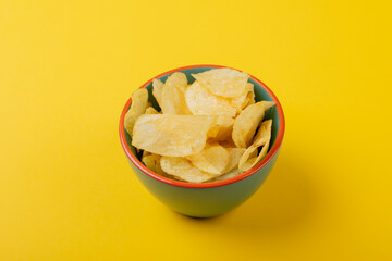 High angle close-up of potato chips in green bowl on yellow background