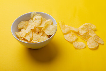 Close-up of potato chips in bowl and on yellow background