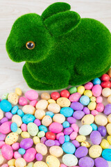 Close-up of artificial moss bunny with colorful candy easter eggs on table