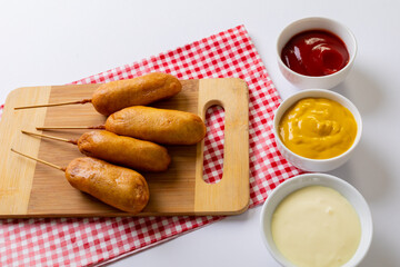 High angle view of corn dogs on serving board with various savory sauces in bowl on table