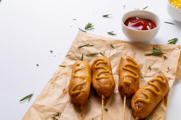 Close-up of corn dogs with mustered sauce and herb on paper bag by tomato sauce in bowl