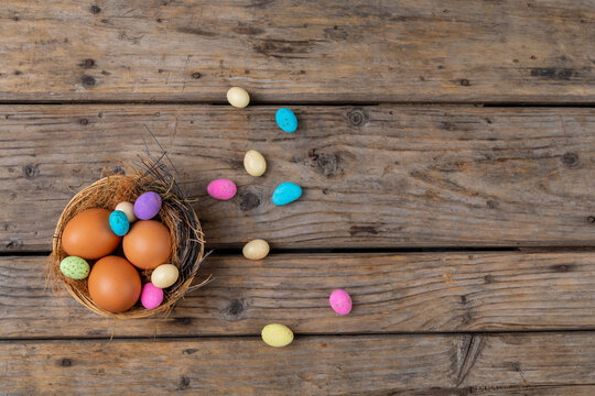 Directly above shot easter eggs and colorful candies in nest on wooden table