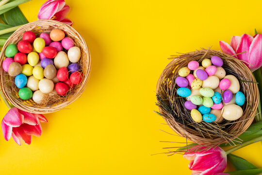 Directly above shot of colorful easter eggs and candies in nests with tulips on yellow background