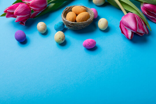 High angle view of easter candies in small nest with pink tulips on blue background with copy space