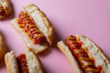 High angle view of yellow and red sauces on hot dogs over pink background