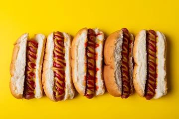 Overhead view of red and yellow sauces on hot dogs arranged side by side over yellow background © wavebreak3