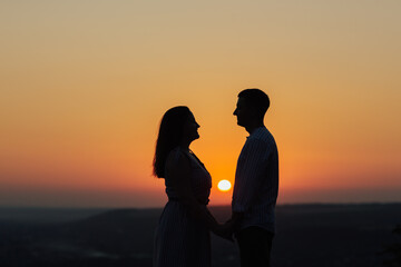 Silhouette of happy couple holding hands and looking each other at summer sunset. Copy space.