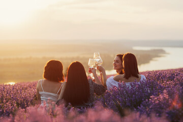 Lovely ladies drinking wine in lavender violet field at sunset. Summer happy mood. Girlfriends...