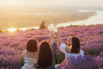 Group of young women having a picnic in the lavender field with wine at sunset.
