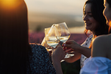Close-up of hands holding glasses with white wine  during sunset. Celebration and friendship concept.