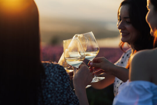 Close-up of hands holding glasses with white wine during sunset. Celebration and friendship concept. - Powered by Adobe