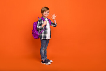 Full size profile side photo of youth cheerful boy wave hi lesson isolated over orange color...