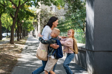 Happy schoolchildren running to their grandmother waiting for them after school outdoors in street.