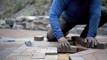 Closeup of hand putting brick paver into place in a hardscaping project.