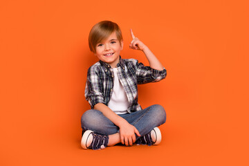 Full size photo of young boy sit floor indicate finger creative choice smart isolated over orange...