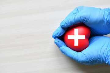 A red cross is a symbol of medical health. Hand holding a heart and on a wooden desk. Copy space...