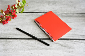 red notepad with black pen and branch of barberry on gray background, close-up