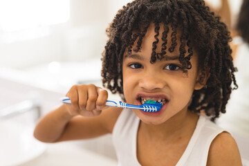 Portrait of hispanic curly haired boy brushing teeth in bathroom at home