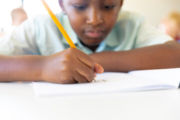 Close-up of african american elementary schoolboy writing on book at desk in classroom