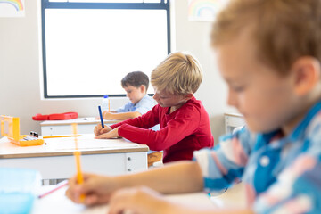 Multiracial elementary schoolboys writing on books while sitting at desk in classroom