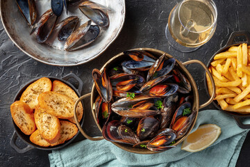 Belgian mussels with French fries and toasted bread, with white wine, overhead flat lay shot on a black background