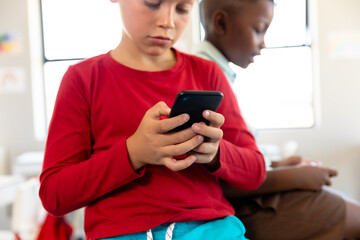 Fototapeta premium Multiracial schoolboys using smartphone while sitting at desk in classroom