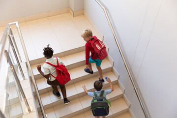 High angle view of multiracial elementary schoolboys with backpack climbing steps in school building