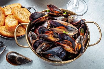 Cooked mussels in a copper pan, Belgian or French cuisine in a restaurant, with toasted bread