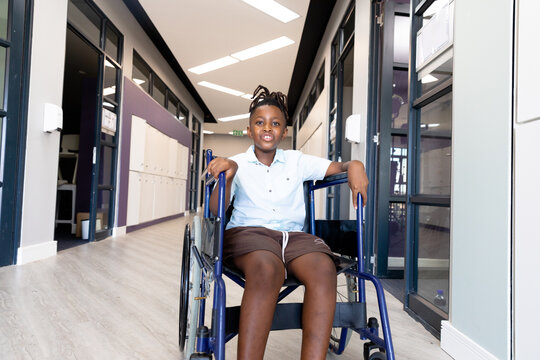 Portrait of african american elementary schoolboy sitting on wheelchair in school corridor - Powered by Adobe