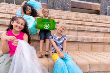 Portrait cheerful multiracial elementary schoolgirls with garbage bags sitting on school steps