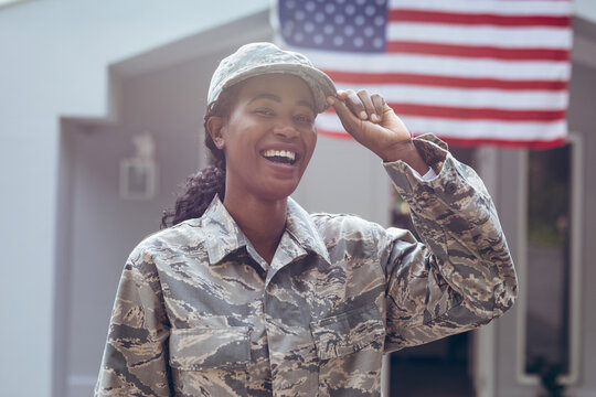 Happy female mid adult african american soldier in uniform standing outside house