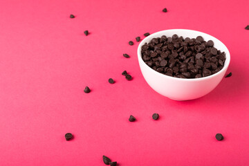 High angle view of fresh chocolate chips full of white bowl against pink background
