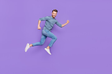 Fototapeta na wymiar Photo of excited attractive guy wear grey shirt running fast jumping high empty space isolated violet color background