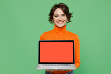 Young smiling happy woman 20s wear casual orange turtleneck hold use work on laptop pc computer...