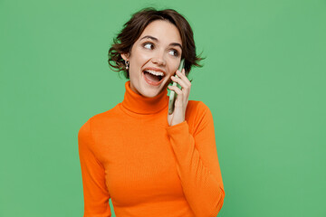 Young smiling happy woman 20s wear orange turtleneck talk speak on mobile cell phone conducting...