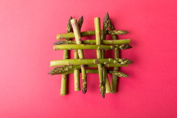 Overhead view of fresh green asparagus stacked on pink background amidst copy space