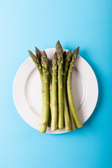 Directly above view of green raw asparagus in white plate over blue background