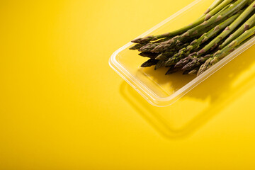 High angle view of raw asparagus in plastic container by copy space over yellow background