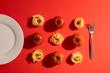  Directly above view of ribbon pasta with tomatoes amidst plate and fork on red background © wavebreak3