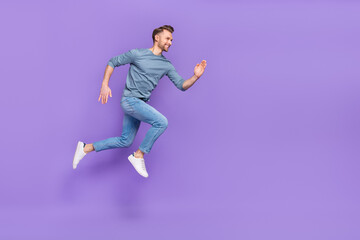 Fototapeta na wymiar Photo of handsome charming guy dressed grey shirt jumping high running fast empty space isolated purple color background