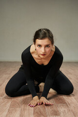 Fototapeta na wymiar a beautiful dancer in black clothes sits on the floor leaning on her palms and knees and looks at the camera