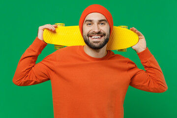 Young smiling happy friendly cheerful fun cool caucasian man 20s wear orange sweatshirt hat hold in hand skateboard isolated on plain green color background studio portrait. People lifestyle concept. © ViDi Studio