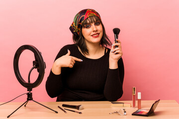 Young makeup artist woman doing a makeup tutorial isolated on pink background person pointing by hand to a shirt copy space, proud and confident