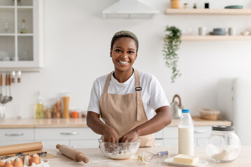 Fototapeta na wymiar Cheerful young african american female chef blogger in apron making pie dough