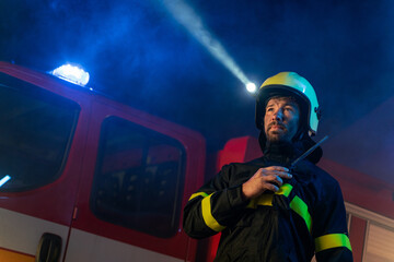 Obraz premium Low angle view of firefighter with fire truck in background at night.
